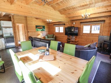 A wooden dining table with green chairs and a living room with black sofas and a television at iLodge 73 in Kenwick near Louth