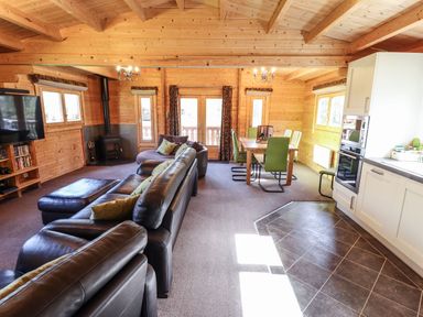 An open plan living room and kitchen with leather sofas a dining table with green chairs a wood stove and white kitchen cabinets at iLodge 73 Kenwick near Louth