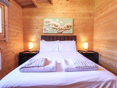 A bedroom with a double bed two bedside tables with lamps and a floral painting on the wooden wall at iLodge 73 Kenwick near Louth