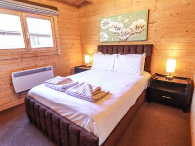 A bedroom with a double bed white linens and towels on the bed between two bedside tables with lamps in a wooden cabin at iLodge 73 Kenwick near Louth