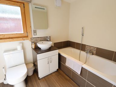 A bathroom with a toilet, sink with cabinet, mirror, bathtub with towel, and wooden framed window at iLodge 73 Kenwick near Louth