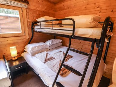 A wooden bedroom with a bunk bed a nightstand with a lamp and a window at iLodge 73 Kenwick near Louth