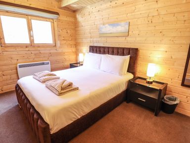 A bedroom with a double bed with white sheets two folded towels bedside tables with lamps wooden walls and a window at iLodge 73 Kenwick near Louth