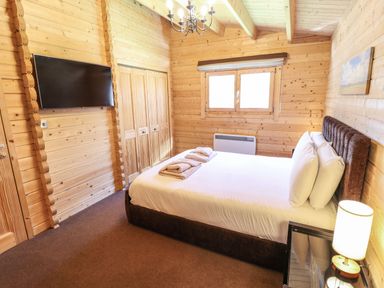 A bedroom with a bed pillows and towels a lamp a wall mounted television and wooden walls at iLodge 73 Kenwick near Louth