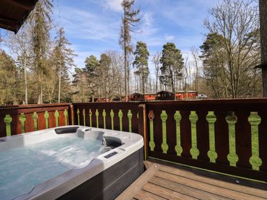 An outdoor hot tub on a wooden deck with a wooden railing and trees in the background at iLodge 73 Kenwick near Louth