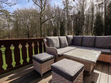 An outdoor deck with wicker furniture including a corner sofa two ottomans and a glass-topped table overlooking trees at iLodge 73 in Kenwick near Louth