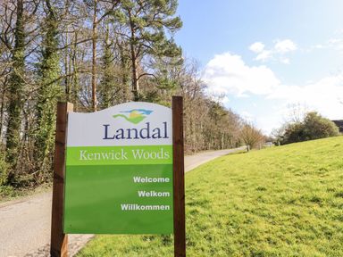 A sign for Landal Kenwick Woods next to a tree-lined road and grassy hill at iLodge 73 Kenwick near Louth