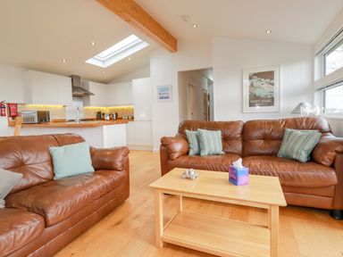 A living room with two brown leather sofas a wooden coffee table and an open kitchen at 10 Faraway Fields in Dobwalls
