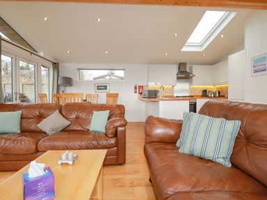 A living room with two brown leather sofas a wooden coffee table wooden dining table and chairs and a kitchen area at 10 Faraway Fields in Dobwalls