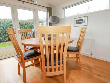A dining room with a round wooden table and wooden chairs with black seats near glass doors and a window at 10 Faraway Fields in Dobwalls