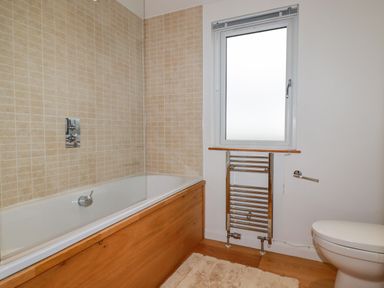 A bathroom with a bathtub with tiled walls a window a chrome towel radiator and a toilet at 10 Faraway Fields in Dobwalls