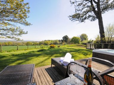An outdoor patio with wicker lounge chairs towels a bottle of wine and glasses overlooking a grassy field and trees at 10 Faraway Fields in Dobwalls