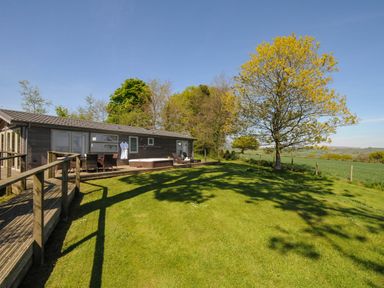 A wooden house with a deck garden furniture and a hot tub on a lawn with a large tree at 10 Faraway Fields in Dobwalls