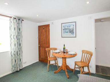 A small dining area with a wooden round table set for two and two wooden chairs at Angel Cottage Weymouth