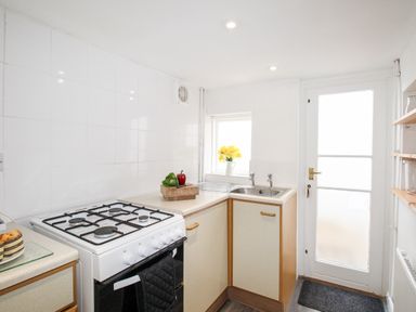 A kitchen with a gas stove wooden cabinets a sink with faucets a window with yellow flowers and a door at Angel Cottage in Weymouth