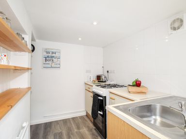 A kitchen with a gas stove kettle toaster sink and shelves with mugs at Angel Cottage in Weymouth
