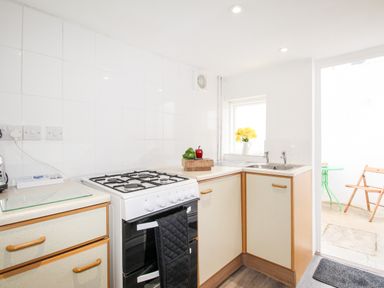 A kitchen with a gas stove sink and cupboard with flowers on the windowsill and a small table and chairs outside at Angel Cottage in Weymouth