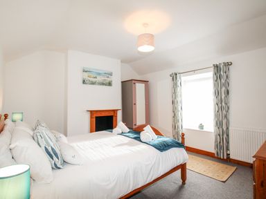 A bedroom with a double bed beside a window with patterned curtains and a wooden wardrobe at Angel Cottage in Weymouth