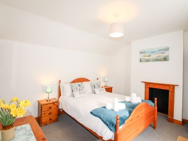 A bedroom with a wooden bed frame bedside tables with lamps a fireplace and flowers on a table at Angel Cottage in Weymouth