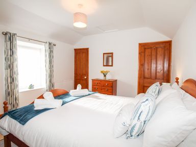 A bedroom with a double bed two wooden doors a chest of drawers with flowers and a window with patterned curtains at Angel Cottage in Weymouth