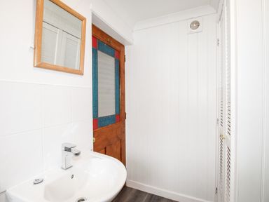 A bathroom with a white sink and faucet a wooden door with stained glass and a wall-mounted mirror at Angel Cottage in Weymouth
