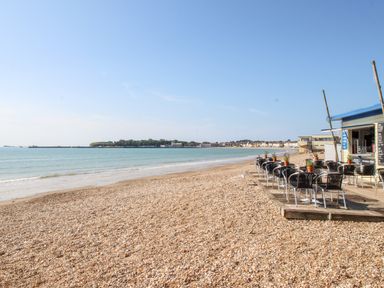 A pebble beach with tables and chairs on a wooden deck near a small beach cafe at Angel Cottage in Weymouth