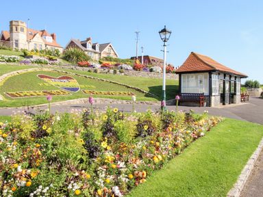 A garden with colorful flowers and a heart-shaped floral display with text next to a small pavilion and lampposts at Angel Cottage in Weymouth