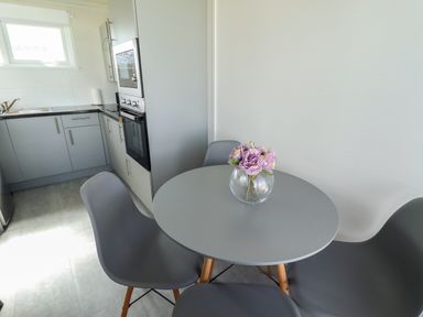A kitchen with gray cabinets a gray round table with pink flowers in a vase and gray chairs at 23 Cherry Park in Chapel St Leonards