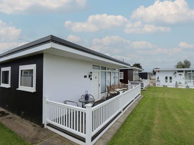 A row of black and white static caravans with outdoor seating and white picket fences on a lawn at 23 Cherry Park in Chapel St Leonards