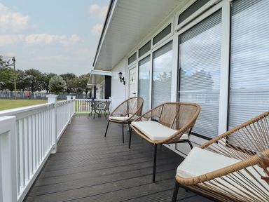 An outdoor balcony with wicker chairs and a small table with two chairs at 23 Cherry Park in Chapel St Leonards