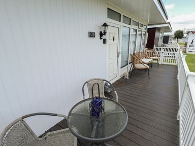 An outdoor deck with a round glass table and chairs outside a white door at 23 Cherry Park in Chapel St Leonards