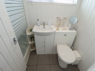 A small bathroom with a sink unit and toilet next to a shower cubicle at 23 Cherry Park in Chapel St Leonards
