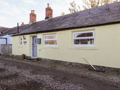 The exterior of a single-story yellow cottage with two windows a gray door and two chimneys at Garden Cottage in Chathill near Beadnell
