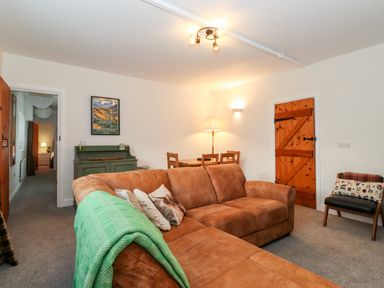 A living room with a brown sofa green cabinet wooden dining table and wooden door at Garden Cottage in Chathill near Beadnell