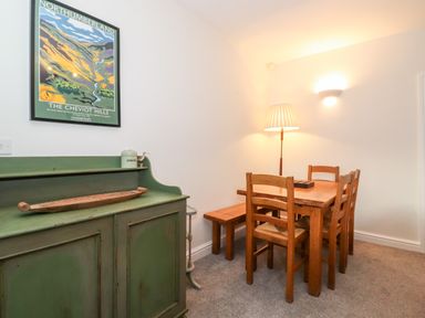 A dining area with a wooden table chairs and bench a green cabinet and a framed Northumberland poster at Garden Cottage in Chathill near Beadnell