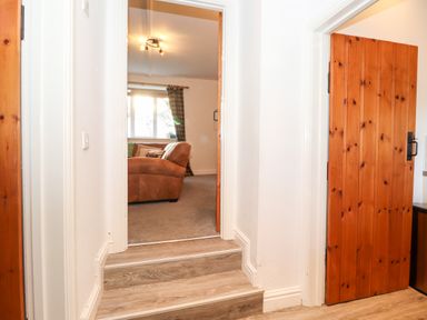 A hallway with wooden doors and steps leading to a room with a brown sofa at Garden Cottage in Chathill near Beadnell