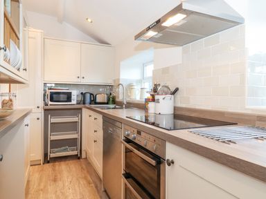 A kitchen with white cabinets a stove oven microwave kettle and toaster at Garden Cottage in Chathill near Beadnell