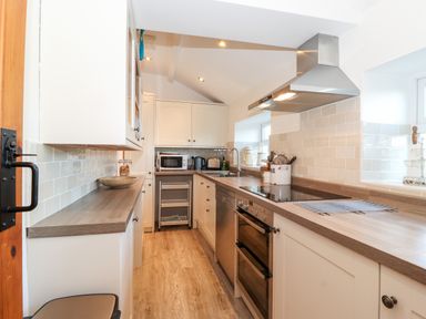 A narrow kitchen with wooden countertops appliances and white cabinets at Garden Cottage in Chathill near Beadnell