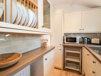 A kitchen counter with a wooden bowl plates in a rack microwave kettle toaster and a rolling storage cart at Garden Cottage in Chathill near Beadnell