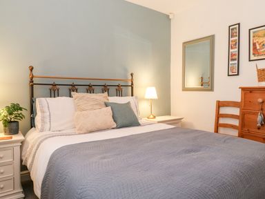 A bedroom with a bed a plant on a bedside table a lamp a mirror chair and wooden dresser at Garden Cottage in Chathill near Beadnell