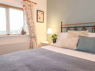 A bedroom with a bed pillows and a bedside table with a lamp and plant at Garden Cottage in Chathill near Beadnell