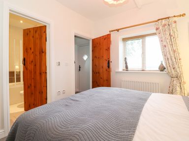 A bedroom with a bed covered by a gray blanket a window with floral curtains and wooden doors at Garden Cottage in Chathill near Beadnell
