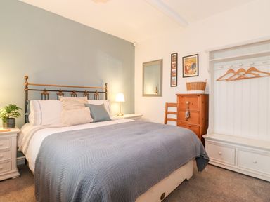 A bedroom with a bed a blue quilt a white nightstand a wooden chair and a white wardrobe at Garden Cottage in Chathill near Beadnell