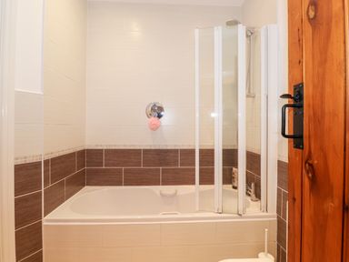 A bathroom with a bathtub shower combination and folding glass shower screen at Garden Cottage in Chathill near Beadnell