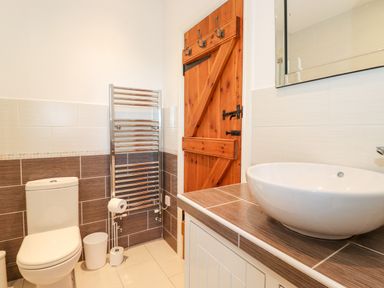 A bathroom with a toilet sink a wooden door and a towel radiator at Garden Cottage in Chathill near Beadnell
