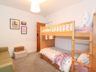 A bedroom with a wooden bunk bed a green sofa wicker baskets and framed pictures on the wall at Garden Cottage in Chathill near Beadnell