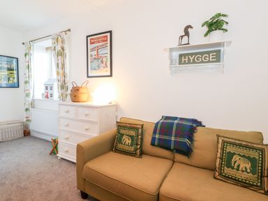A living room with a beige sofa with elephant cushions a chest of drawers and framed posters at Garden Cottage in Chathill near Beadnell