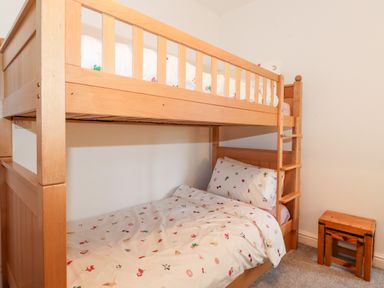 A wooden bunk bed with patterned bedding and a small wooden stool on a carpeted floor in a bedroom at Garden Cottage in Chathill near Beadnell