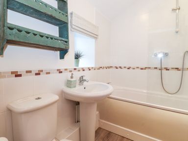 A bathroom with a toilet sink bathtub shower and a green wall shelf with a potted plant at Garden Cottage Chathill near Beadnell