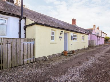 A row of single-story cottages with gravel path and wooden gates at Garden Cottage in Chathill near Beadnell